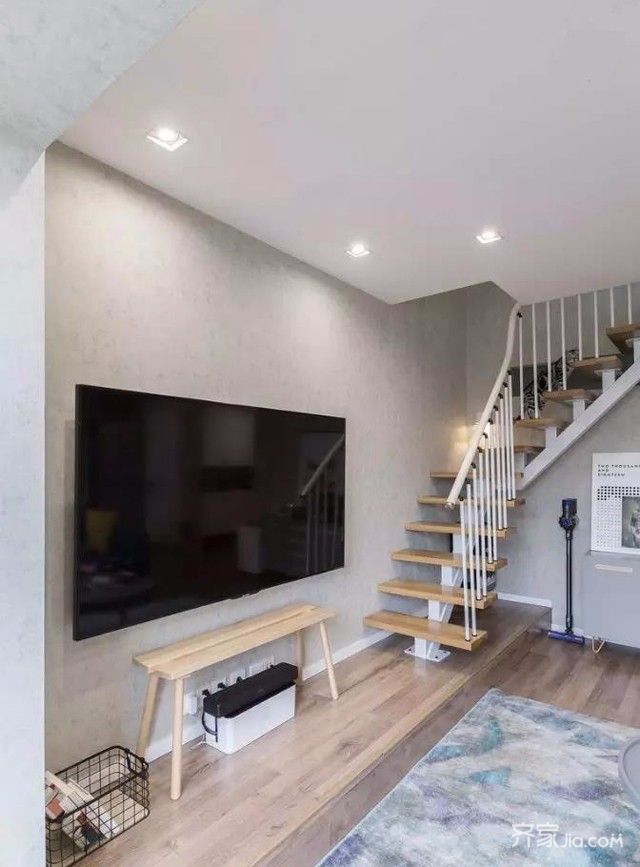 的客厅区域,电视墙简单素色壁纸,条凳充当电视柜,侧墙就是楼梯空间