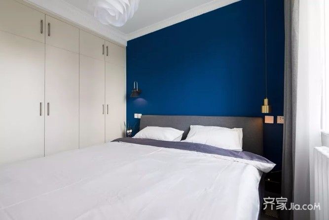 卧室以深蓝色的背景墙,搭配一张灰色布艺床,床头两侧都做了吊灯,布置